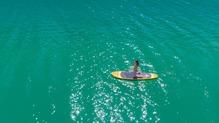une jeune fille à genou sur son stand up paddle jaune , au milieu d'eau verte