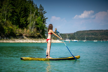 une jeune fille en maillot de bain rouge se tient debout sur un stand up paddle jaune 