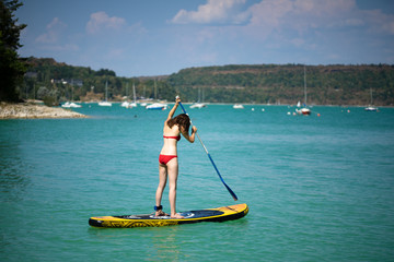 une jeune fille en maillot de bain rouge debout en &eacute;quilibre sur un stand up paddle jaune 