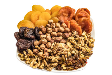 Nuts and dried fruits on a white plate. Set of peeled hazelnuts, walnuts kernels, raisins and dried apricots of different kinds.