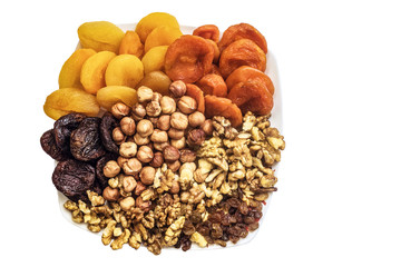 Nuts and dried fruits on a white plate. Top view and copy space. Set of peeled hazelnuts, walnuts kernels, raisins and dried apricots of different kinds.