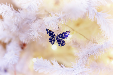 Bright decorations of a glass mosaic butterfly on a white Christmas tree. Festive background for design, copy space. Selective focus. Winter holiday, Happy New Year, xmas.