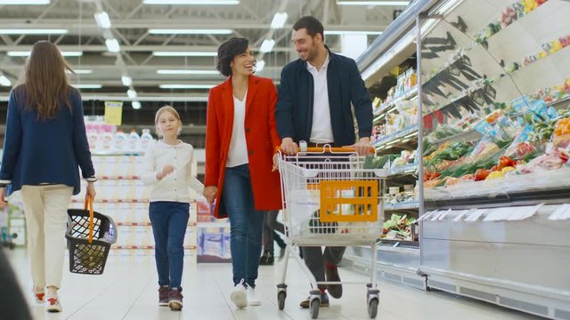 At the Supermarket: Happy Family of Three, Holding Hands, Walks Through Fresh Produce Section of the Store, Holding Hands. Father, Mother and Daughter Having Fun Time Shopping.