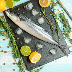Fresh mackerel on a black slate stone with spices, herbs, lemon, lime and salt. View from above