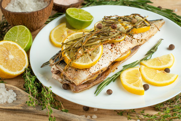 Cooked mackerel on a white plate with spices, herbs, lemon, lime and salt. A close-up, on a wooden background.Concept of homemade food, and tasty healthy food