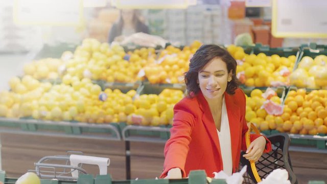 At the Supermarket: Portrait of the Beautiful Smiling Woman Choosing Organic Fruits In the Fresh Produce Aisle and Puts them into Shopping Basket. High Angle Shot.