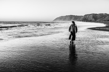 Beautiful young girl walking with it wet ankles along the sea water on an amazing wild beach during a sunny day at sunset time in Topocalma Beach, Puertecillo, Chile