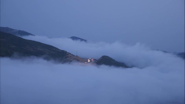 Clouds rolling around a mountain peak with morning commutes in the middle.