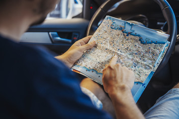 Close up of young man looking at map behind the wheel in car.