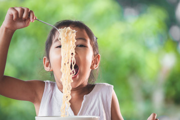 Cute asian child girl eating delicious instant noodles with fork in the nature background