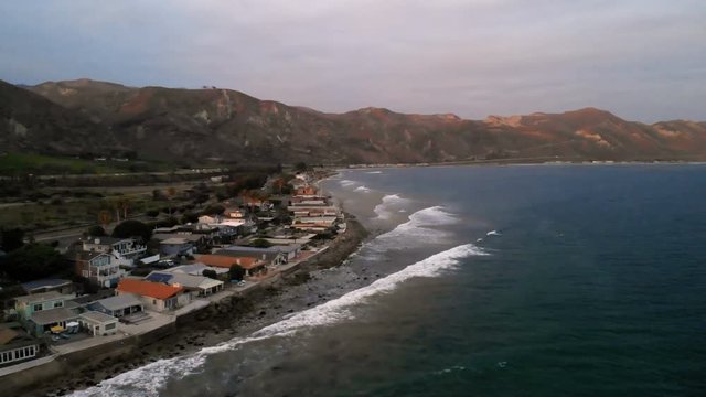 Aerial view of beach houses along Pacific Coast in California.  Real estate during sunset. From above, drone flying over water.
