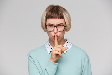 Closeup of serious strict young woman wears blue sweatshirt and spectacles looks displeased and...