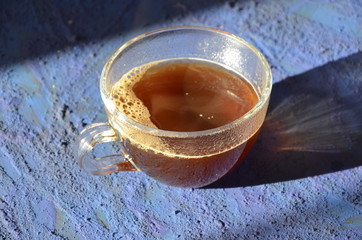Transparent cup of coffee placed on dark blue surface in front of a window. glass cup with hot black coffee on a dark background with steam
