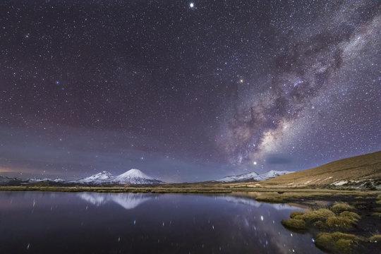 The great "Nevados de Payachatas" with the Pomerape and Parinacota Volcanoes, left and right respectively and the Milky Way galactic core rising from the East over Cotacotani Lagoon waters, Arica, Chi