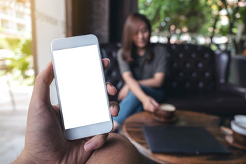 Mockup image of hand holding white mobile phone with blank screen in cafe and woman in background
