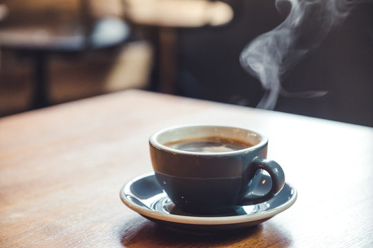 Closeup image of a blue cups of hot coffee with smoke on vintage wooden table in cafe