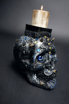 Skull decorated with colorful stones with candle on black background