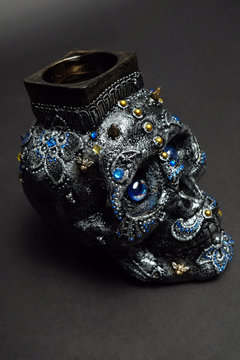 Skull decorated with colorful stones with candle on black background