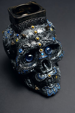Skull decorated with colorful stones with candle on black background