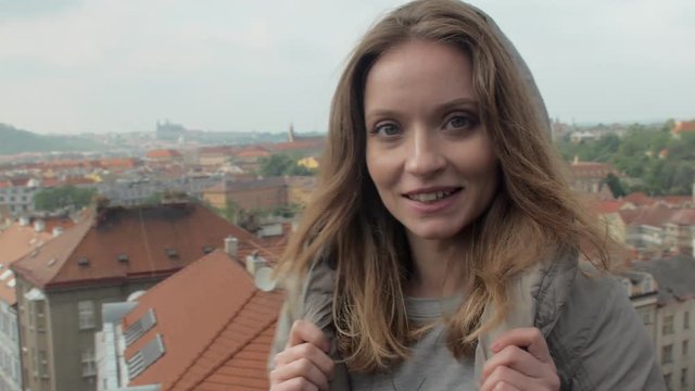 young woman is looking on Prague panorama, turning to camera and smiling