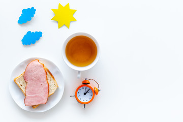 Parts of day. Morning. Time for breakfast. Tea, sandwich near alarm clock, sun and clouds cutout on white background top view copy space