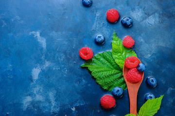 Summer berries in wooden spoons top view. Raspberry and blueberry mix on a dark blue wet background with copy space. Raw ingredients from above