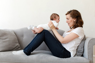 Fototapeta na wymiar Side view of woman sitting on couch at home with newborn baby on hands