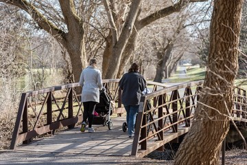 two young moms pushing strollers in park in early spring