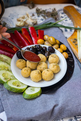 Woman hands adds tomato sauce to buddha bowl with chickpea falafel balls, tomato sauce, olives, cucumbers, red pepper. Vegan vegetables lunch, vegetarian dinner, healthy dietary food
