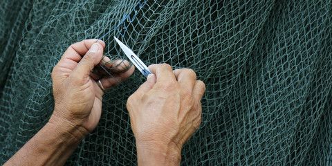 Hand of fisherman repair a net with a knife 