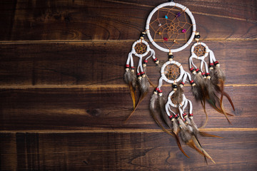 Fototapeta premium Dream catcher with feathers threads and beads rope hanging spiritual folk american native indian amulet isolated on brown wooden textured background.Concept prevent evil in Halloween.