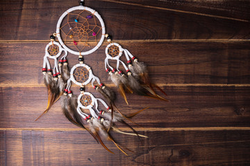 Dream catcher with feathers threads and beads rope hanging spiritual folk american native indian amulet isolated on brown wooden textured background.Concept prevent evil in Halloween.