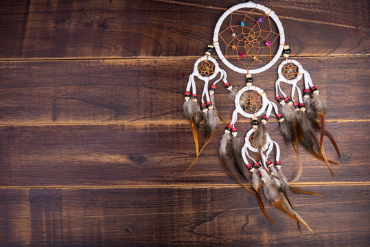 Dream catcher with feathers threads and beads rope hanging spiritual folk american native indian amulet isolated on brown wooden textured background.Concept prevent evil in Halloween.
