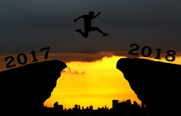 A young man jump between 2017 and 2018 years over the sun and through on the gap of hill silhouette evening colorful sky. happy new year 2018.