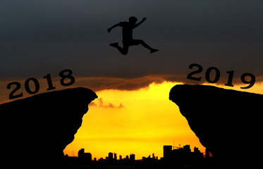 A young man jump between 2018 and 2019 years over the sun and through on the gap of hill  silhouette evening colorful sky. happy new year 2019.