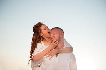 funny pretty girl with dreadlocks biting her cute boyfrieng sitting on his back