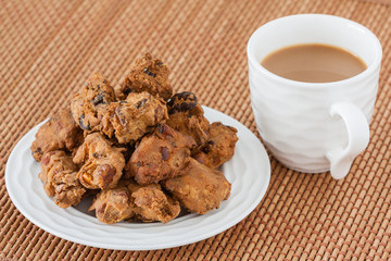Indian pakoda snack with coffee - A macro closeup of traditional deep fried Indian snack pakkoda on a plate served with coffee. A variety of nuts and flour is used to prepare it.