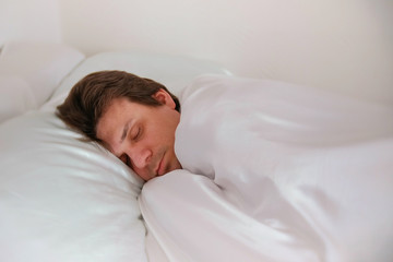 Fototapeta na wymiar Man is sleeping in bed alone under the blanket. Side view.
