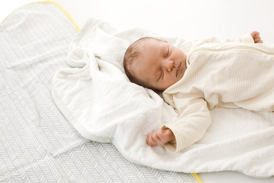 From above shot of tiny newborn baby sleeping on white soft blanket in light