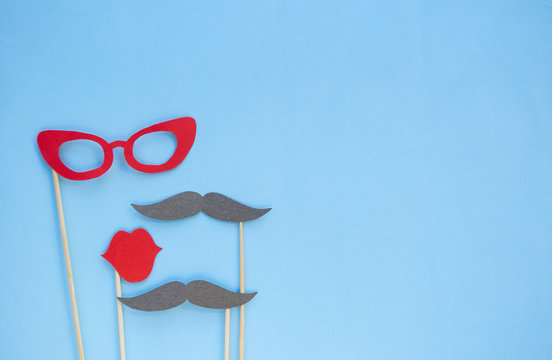 Colorful photo booth props glasses, lips and moustaches on blue background with copyspace.