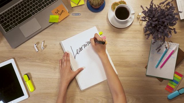 Girl writes on a piece of paper a phrase - Learning Spanish, sitting at work table, first-person view of hands.