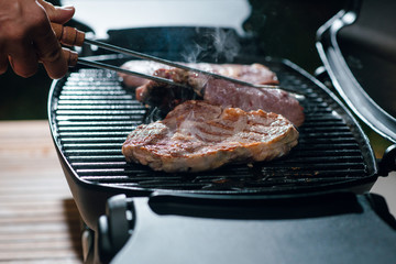 Close up man cooking steaks on the grill for dinner. Outdoors on the backyard.