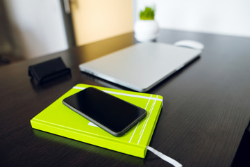 Business concept. Closed laptop computer and black smartphone on the black wooden table at the office.