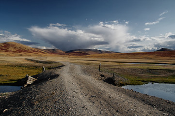 Road through a dry desert steppe on a highland mountain plateau with yellow green grass with ranges of hills rocks on a horizon skyline