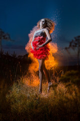 A girl in a black top and red skirt jumping and dancing in a field during photoshoot with flour and light behing her