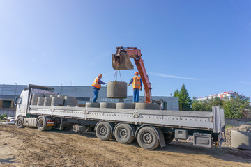 Delivery and unloading of construction materials by the excavator to the construction site. Concrete rings and elements for a well.