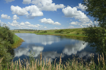 Sunny summer landscape with river,fields,green hills and beautiful clouds in blue sky.