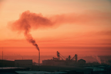 Smoke from pipe pollutes environment in dawn. Storage of goods in warehouses in winter. View from above of industrial area in sunrise in pink tones. Industrial buildings zone close up with copy space.