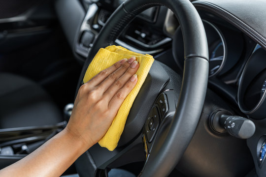 hand cleaning steering wheel of car with microfiber cloth