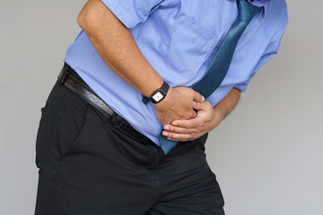 Man holding his stomach in pain on gray background. Businessman suffering from abdominal pain. Body And Health Care Concept.